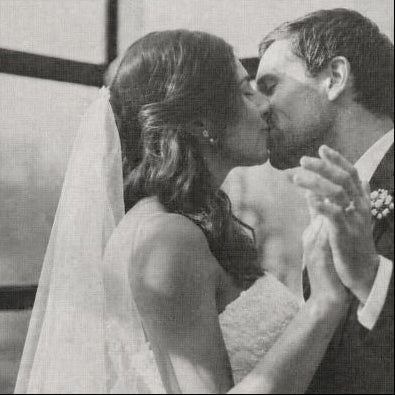 Black and white photo of a bride and groom kissing in front of a church.